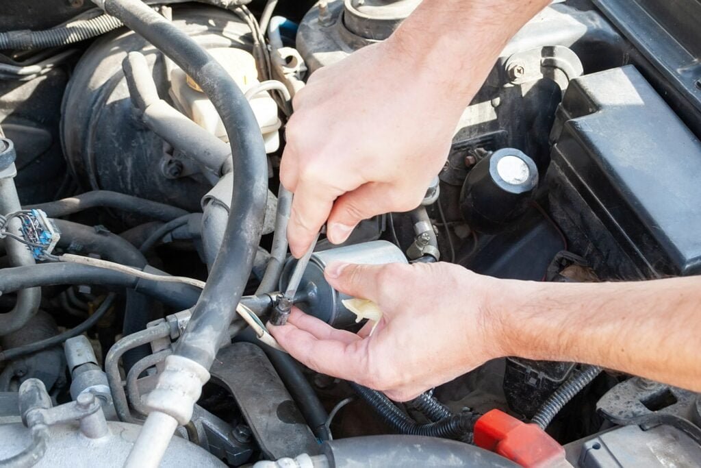 Male hands unscrew fuel line from fuel filter with screwdriver